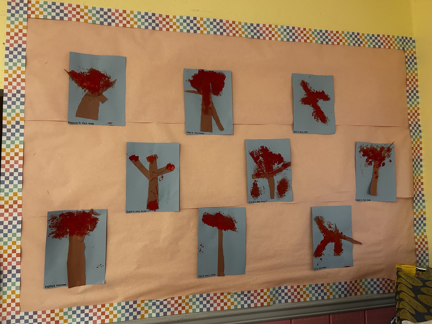 Children’s fall tree artwork with red painted leaves and brown paper trunks displayed on a classroom bulletin board.