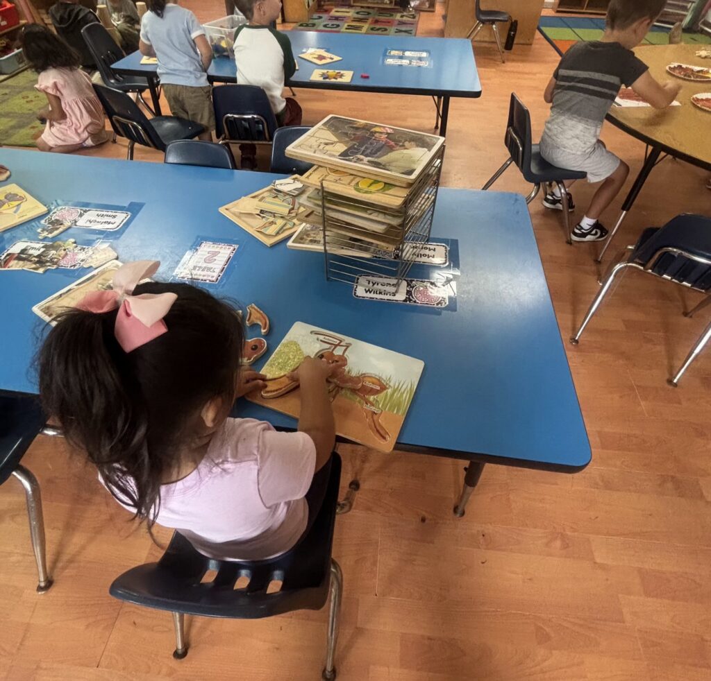 Child working on a wooden puzzle at a blue classroom table