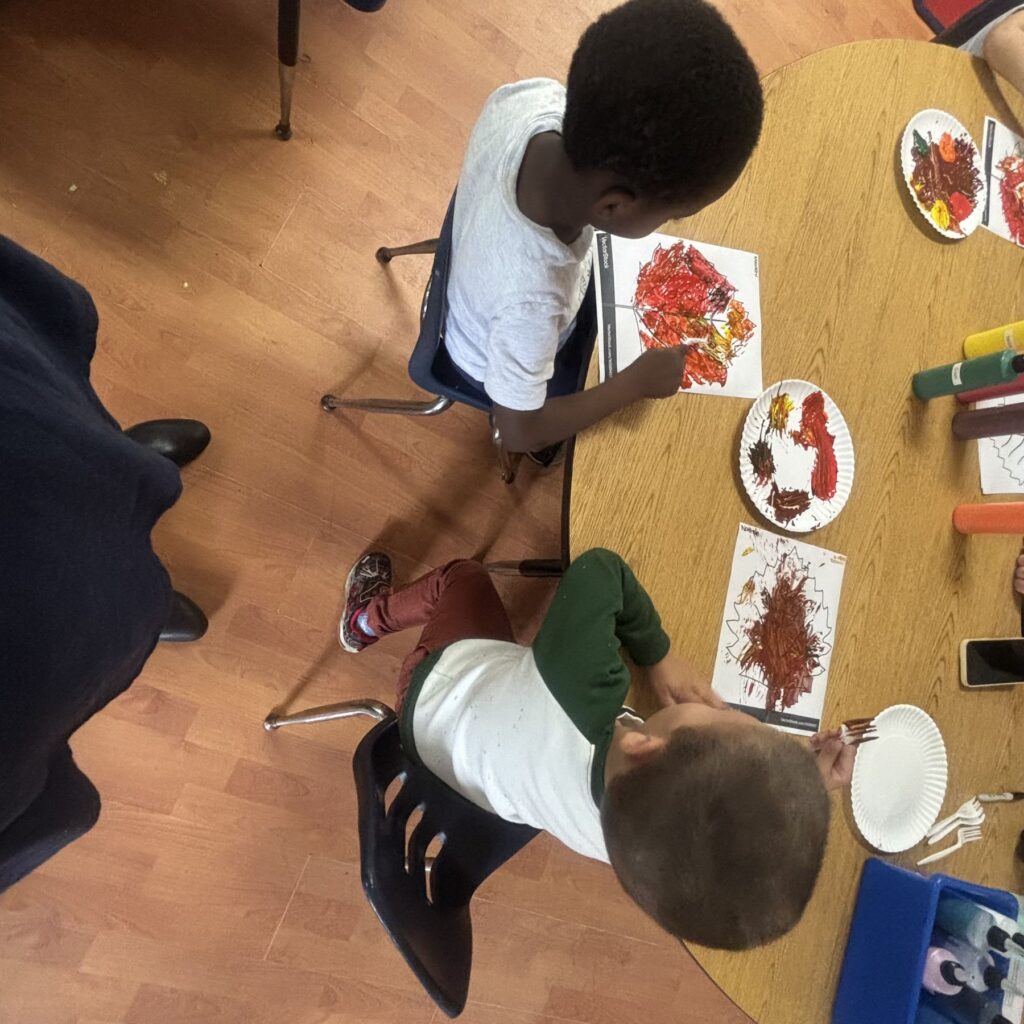 Children stamping autumn tree paintings at the art table